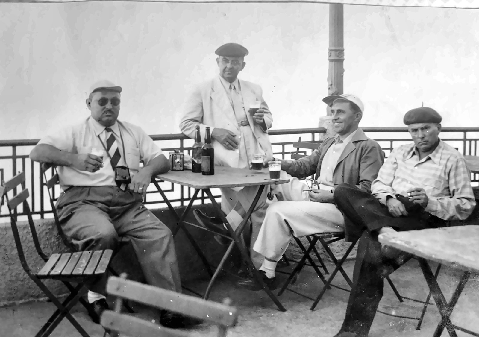 Quatro homens de boina e chapéu numa mesa de café, foto em preto e branco
